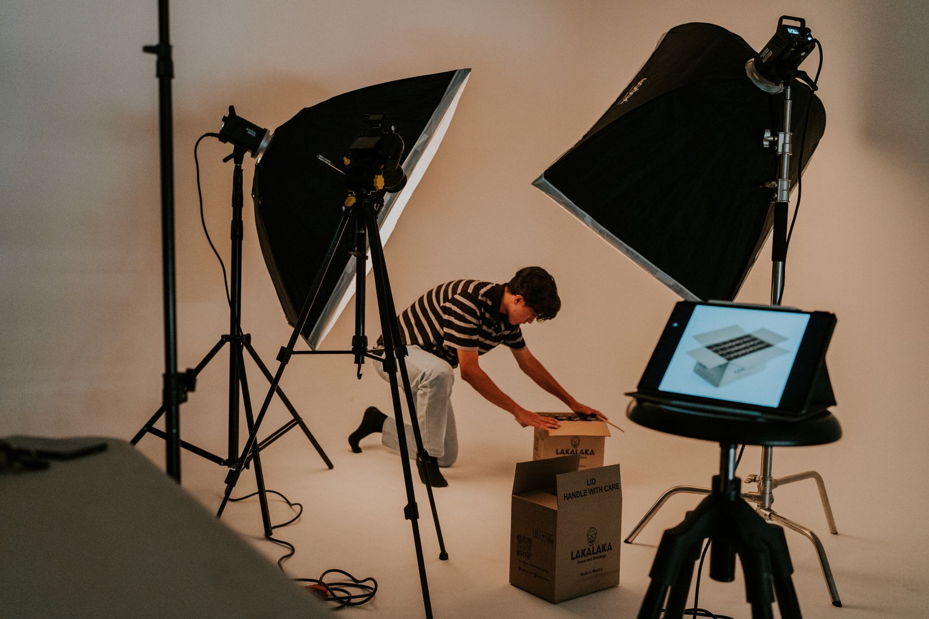 Een man maakt pakketten klaar in een fotostudio met softboxen, statieven en een tablet op een kruk