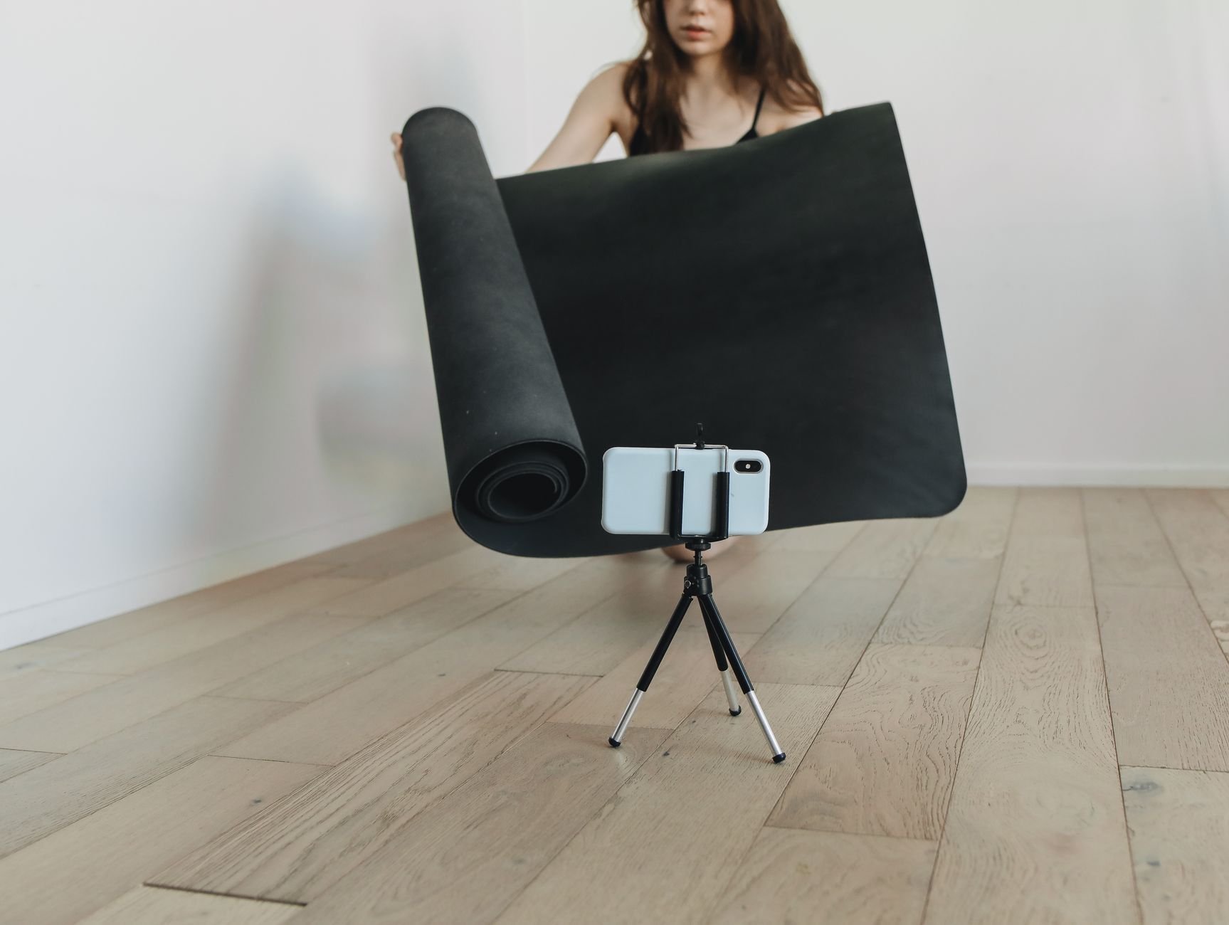 Een vrouw rolt thuis een zwarte mat uit terwijl haar smartphone op een klein statief staat te filmen